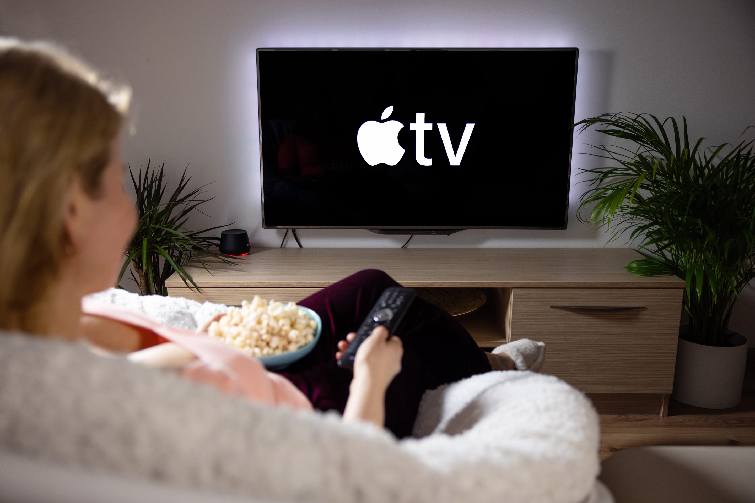 Riga, Latvia – April 14, 2021: Woman watching television at home, Apple TV logo on the screen.